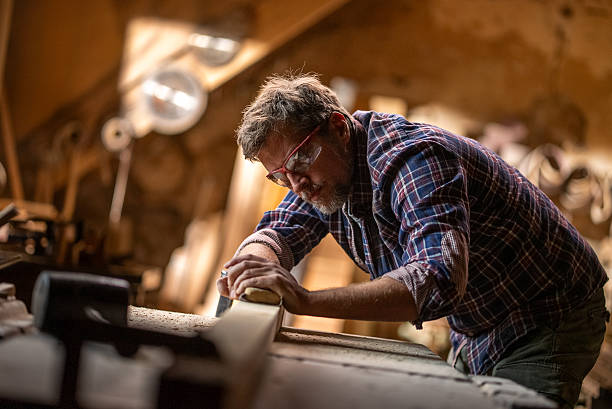 istock Carpenter sanding wood plank in workshop with safety glasses 2215962647