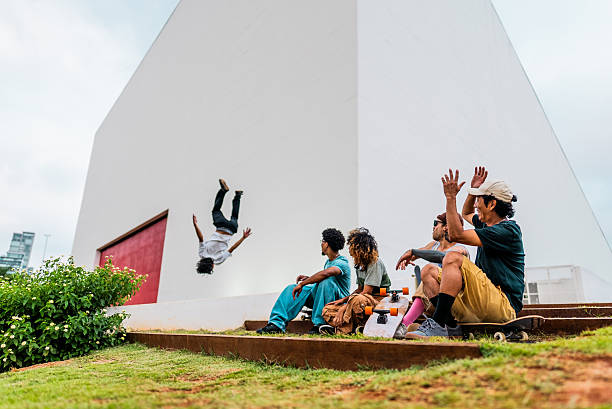 Group of friends sitting on outdoor steps, reacting with excitement as one of their friends performs a backflip in the background. The scene conveys adrenaline, fun, and friendship in a contemporary urban setting