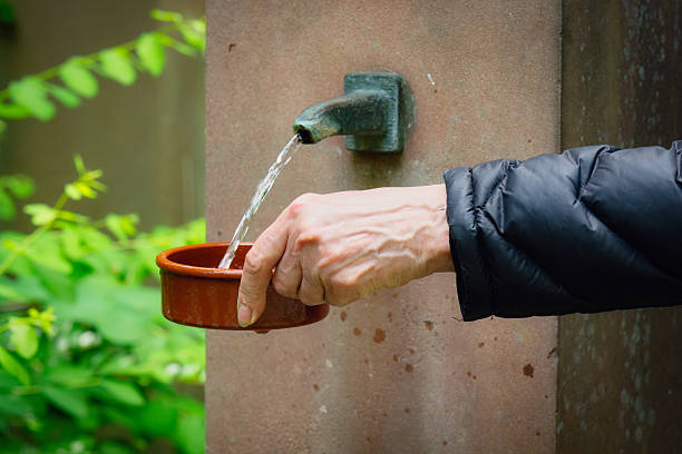 close-up of a hand filling a shallow ceramic vessel from a wall fountain in a cemetery with water as a drinking trough for insects and animals