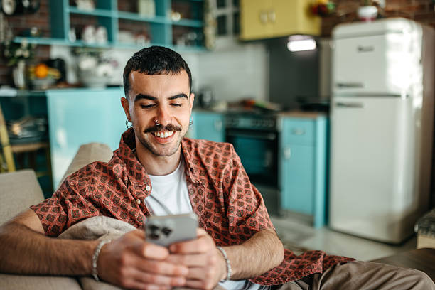 istock Cheerful hipster man using smart phone while relaxing on a sofa at home 2215969655