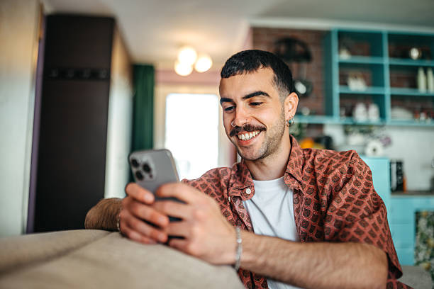Cheerful hipster man using smart phone while relaxing on a sofa at home