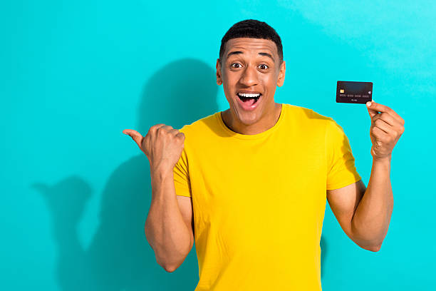 istock Portrait of handsome astonished man hand hold plastic debit card indicate finger empty space isolated on teal color background 2215971005