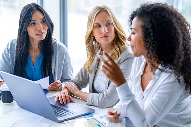 istock Three women meeting in a board room. There is a laptop computer on the table. There is a large window behind them. 2215971438