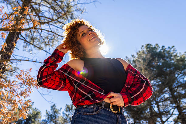 Smiling young woman with curly red hair enjoying sunlight during a hiking trip in a forest