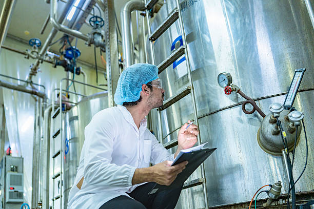 istock Factory technician inspecting an industrial tank with a clipboard, showcasing precision, quality control, and attention to detail in a modern manufacturing environment. 2215974956