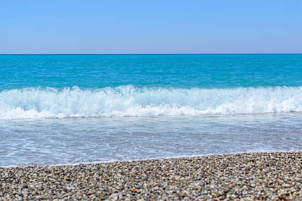 Serene turquoise sea meeting a pebbled beach under a clear blue sky. Represents tranquility, vacation, or escape. Ideal for travel or relaxation themes.
