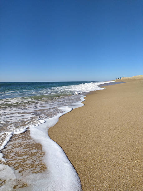 istock Serene ocean scene. Waves gently washing ashore on a sandy beach under a clear blue sky. Evokes tranquility and peaceful escape. Great for travel or relaxation. 2215982402