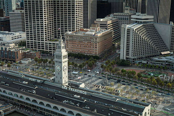 High angle drone shot of the stars and stripes flying from the clock tower of the Ferry Building on the Embarcadero in San Francisco, California.