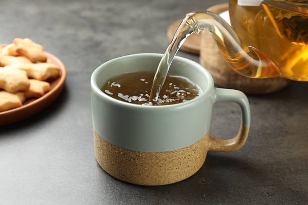 istock Pouring tasty tea into cup at grey table indoors, closeup 2215997035