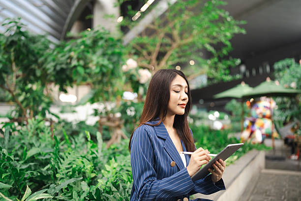 istock Young woman thoughtfully sketches notes or ideas on her tablet amidst lush greenery, blending innovation with tranquility in a vibrant urban setting. 2216007740