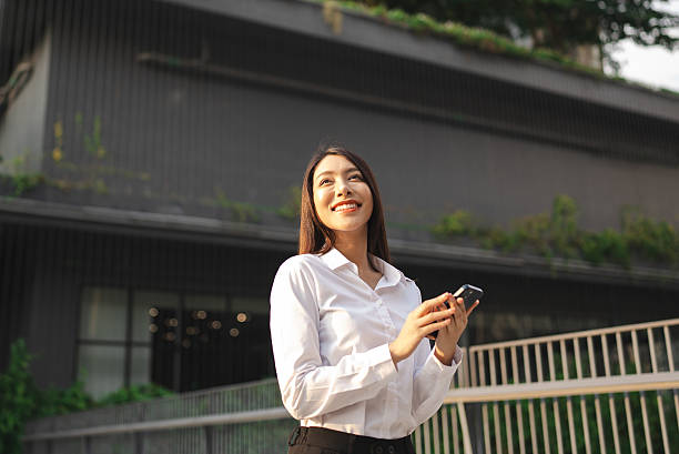 istock Young professional pauses thoughtfully, smartphone in hand, as sunlight gently illuminates her smiling face, 2216007840