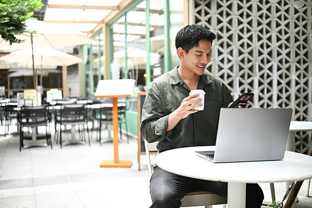istock A man is sitting outside at a small table, deeply engrossed in his laptop while also enjoying a cup of coffee 2216008939