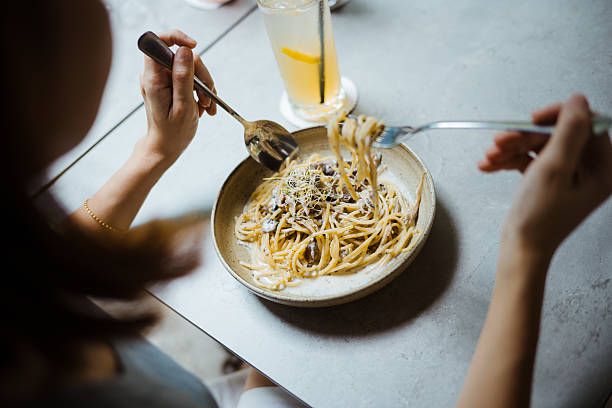 istock Rear View of a woman using spoon and fork to eat carbonara spaghetti on table 2216012990