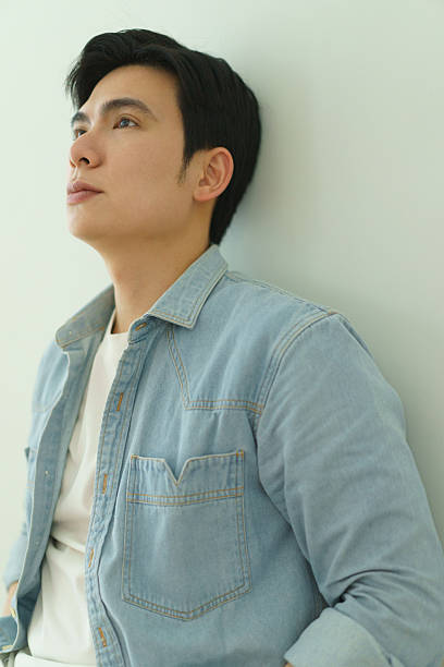 istock Pensive Young Man in Casual Denim Shirt Leaning Against a Wall 2216013921
