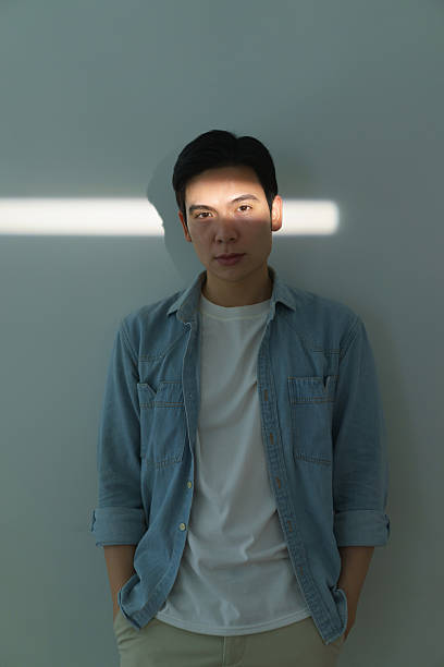 istock Young Man Standing Against Wall With Beam of Light on Face 2216013945