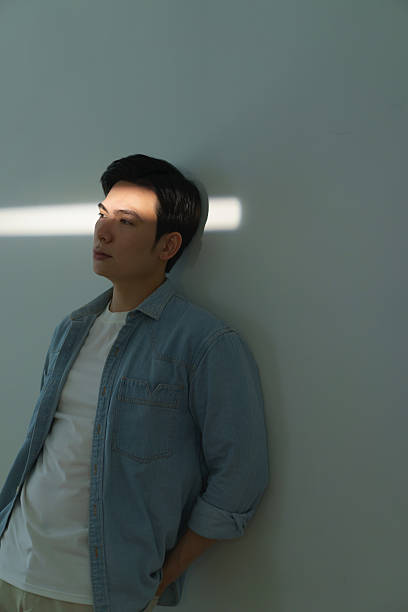 istock Young Man in Denim Shirt Relaxing Against Neutral Wall 2216013950