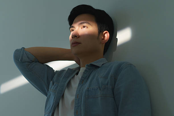 istock Man Relaxing Against Wall With Sunlight Streaming on His Face 2216013951