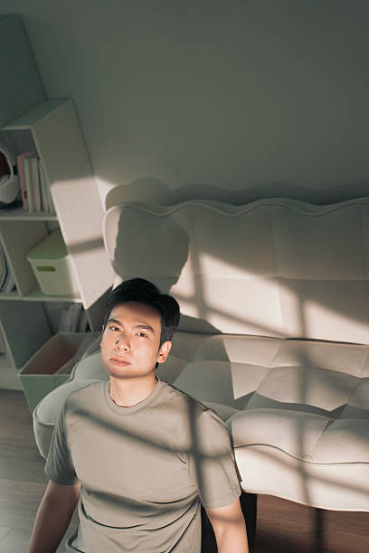 istock Young Man Sitting on Floor Near Sofa in Soft Natural Light 2216013988