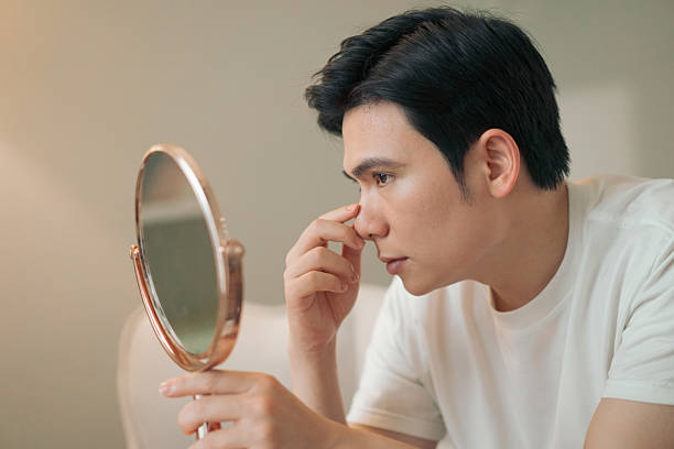 istock Man Examining His Face Closely in a Mirror Indoors 2216014018