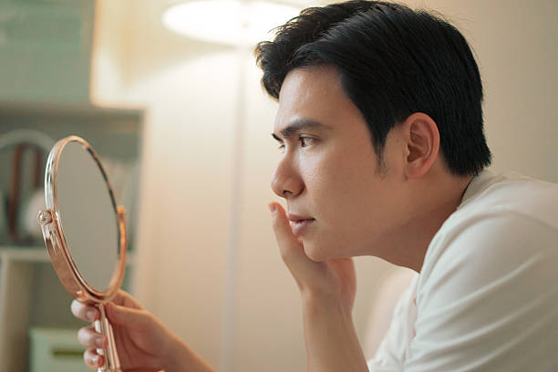 Man Examining Himself in a Handheld Mirror at Home