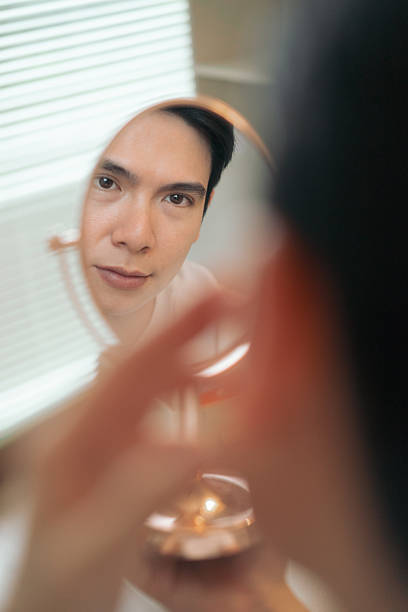 istock Man Looking at Reflection in Handheld Mirror in Brightly Lit Room 2216014025