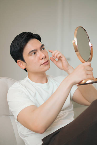 istock Man Examining His Face With A Hand Mirror Indoors 2216014034
