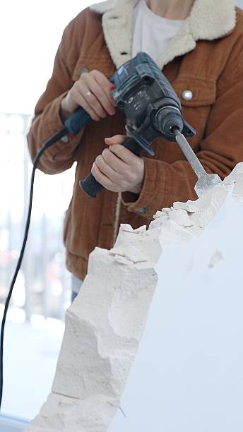 istock Unknown female construction worker demolishing concrete wall with rotary hammer, wearing protective safety gear. Renovation concept, closeup vertical view 2216015854
