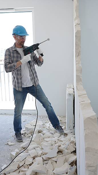 istock Man construction worker demolishing a wall with a hammer drill in protective gear, creating construction debris on the surrounding floor surface. Renovation concept 2216016775