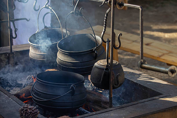 istock Traditional cast iron pots and kettle hanging over an open fire pit with rising smoke at outdoor historical camp 2216018103