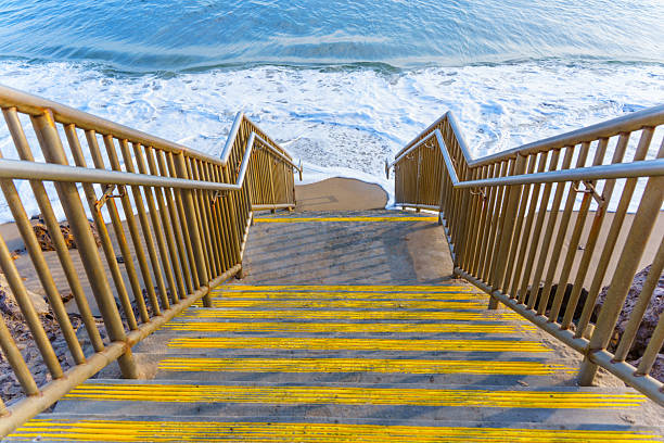 Staircase with vibrant yellow markings leads towards sandy Malibu beach, where gentle ocean waves create a calming retreat for beachgoers.
