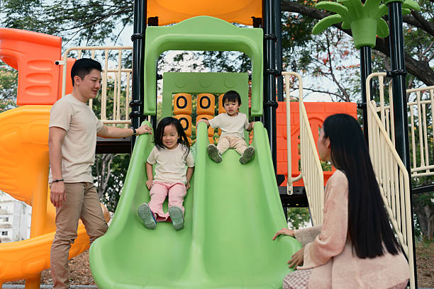 istock Smiling siblings enjoy a fun ride down a double slide as their parents stand by 2216021056