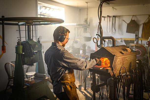 istock Mid-Adult Male Blacksmith Heating Metal in Forge in Workshop with Warm Lighting 2216021441