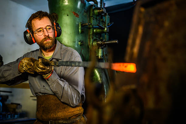 istock Mid-Adult Blacksmith In Gray Workwear And Leather Apron Working At Industrial Forge Workshop 2216021443