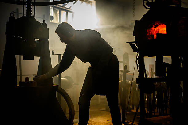 istock Focused Blacksmith Shaping Metal with Hydraulic Press in Dimly Lit Workshop 2216021449