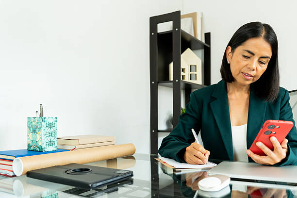 istock Professional businesswoman multitasking, writing notes and checking smartphone during workday at office desk environment 2216024118