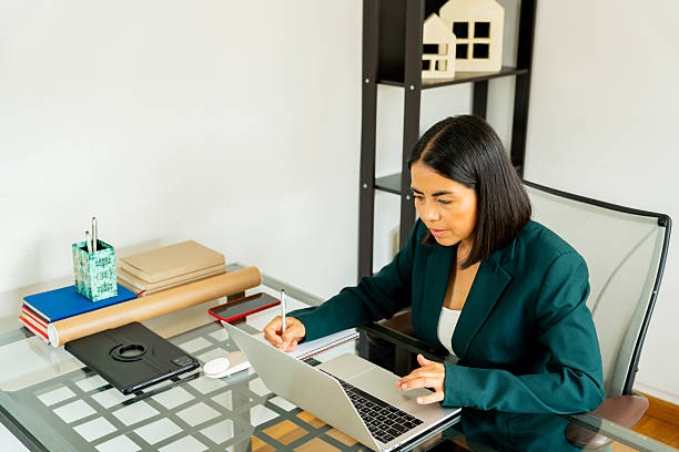 istock Young Latin woman working as an architect from her home office using a laptop and taking notes 2216024164
