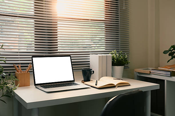 istock Laptop with blank screen by the window with soft sunlight streaming through blinds 2216025113