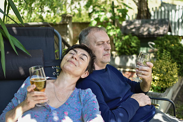 middle aged couple enjoying a nice sunny day in their backyard drinking beer sitting smiling and looking at camera
