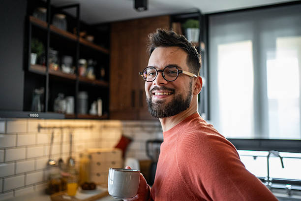 istock Young man smiling and drinking coffee in his modern kitchen 2216032582