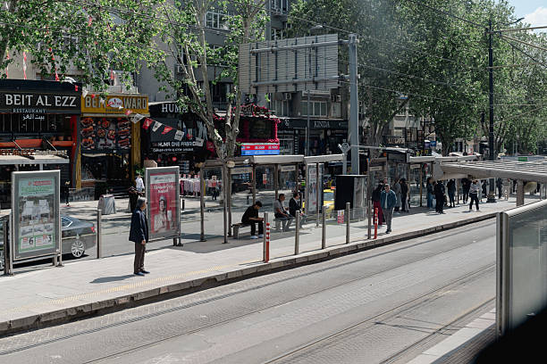 Istanbul, Turkey - May 20 ,2025: A lively street scene in Fatih, a prominent district of Istanbul, Turkey, centered around a tram stop. People are waiting for public transport, while various shops and restaurants line the background, showcasing the daily urban rhythm and the accessibility of public transportation in this bustling area.