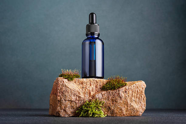 istock Blue glass dropper bottle with pipette standing on natural moss-covered stone 2216037564