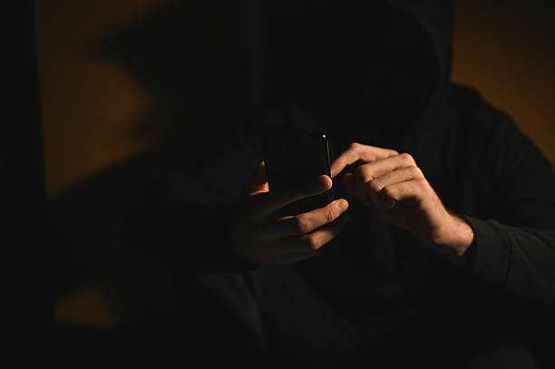 istock Hooded man browsing the internet on his smartphone in the dark 2216050489