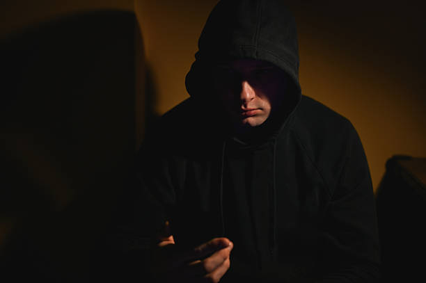 istock Young man wearing hoodie using smartphone in dark room 2216050498