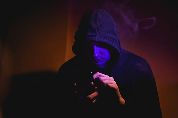 istock Hooded man using smartphone in dark room with purple smoke 2216051025