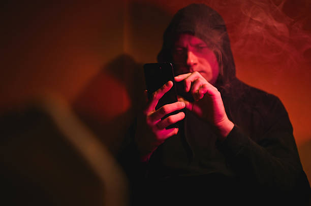 istock Young man browsing smartphone in red-lit room filled with smoke 2216051028