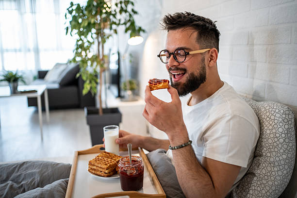 istock Young man enjoying breakfast in bed with waffles and jam 2216051242