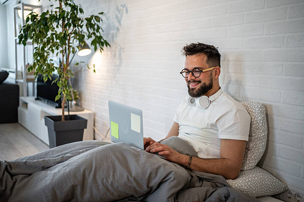 istock Young man working from home sitting in bed using laptop 2216051245