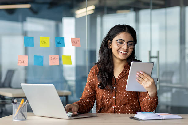 istock Successful businesswoman at workplace smiling, multitasking working with tablet computer, sitting at desk with laptop. Company employee satisfied with results of achievement 2216052049