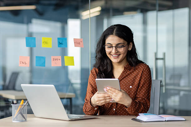 istock Successful businesswoman using tablet computer while sitting at desk with laptop in office. Female consultant employee of company happy and smiling 2216052053