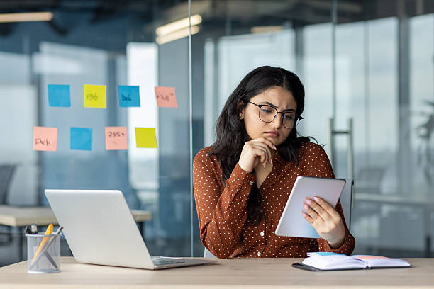 istock Serious thinking woman using tablet computer. Businesswoman multitasking working inside office with notebook. Concentrated female employee reading electronic report online email 2216052054